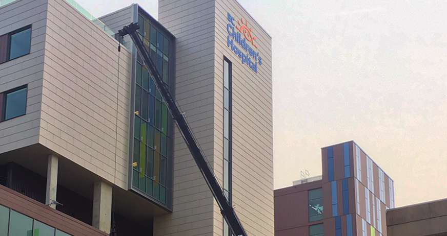 A crane extends towards a modern hospital building with colorful window details on a cloudy day.